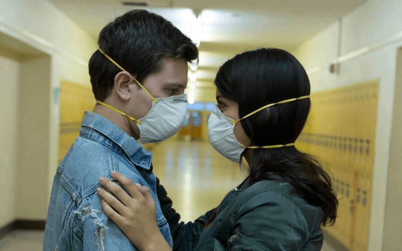 Travis Tope and Sofia Black-D'Elia embrace in a school hallway while wearing masks in the film Viral