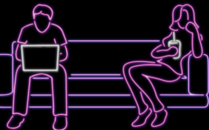 A picture of a couple sitting on opposite ends of a couch. The woman is drinking a soda and the man working at his computer. The picture is made with neon lights.